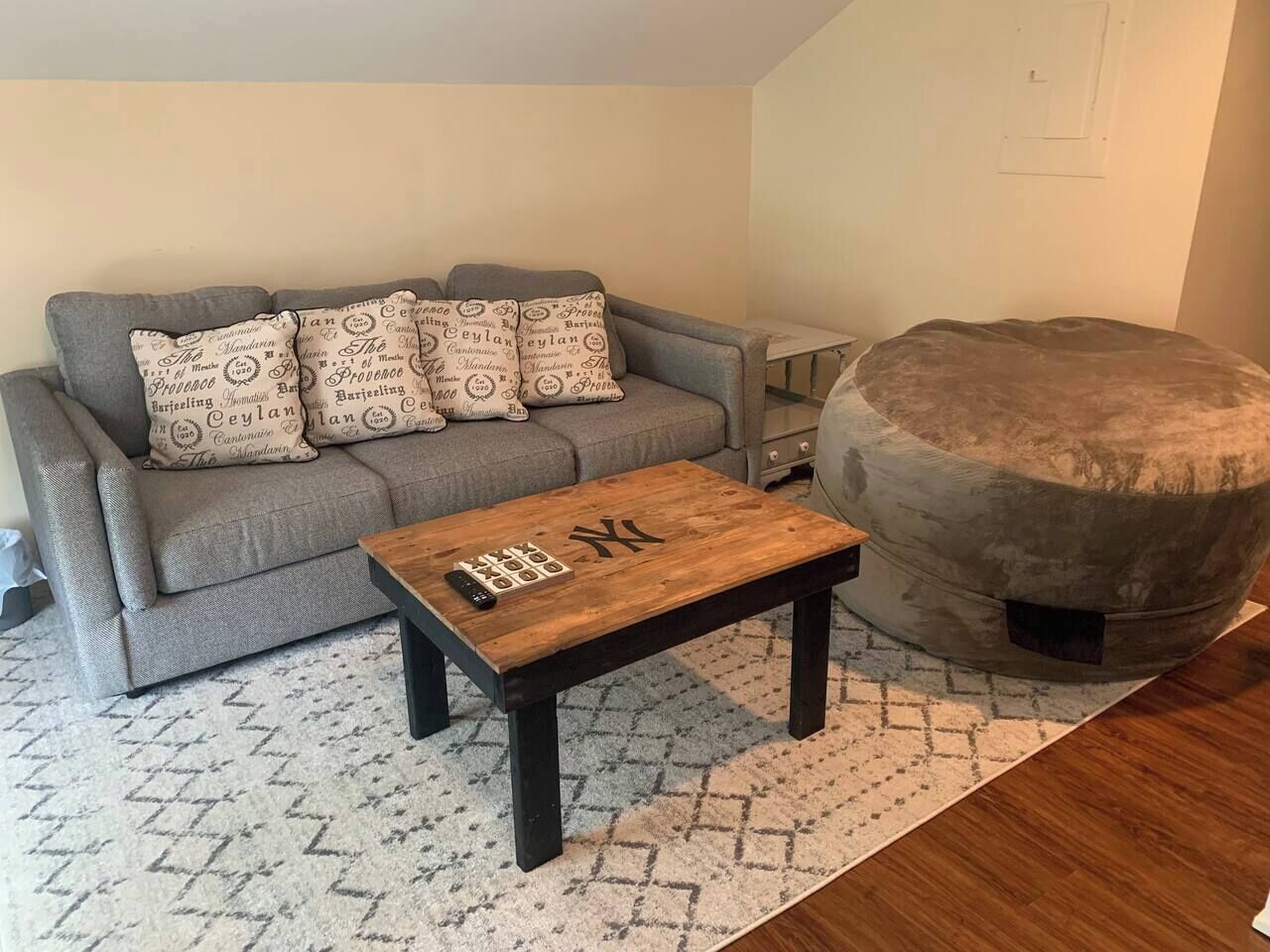Una sala de estar con un sofá gris, cojines estampados, una mesa de centro de madera y un otoman redondo.