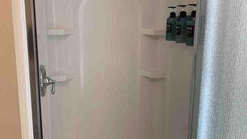 Douchegedeelte met een glazen deur, een douchekop en drie flessen shampoo op een plank.