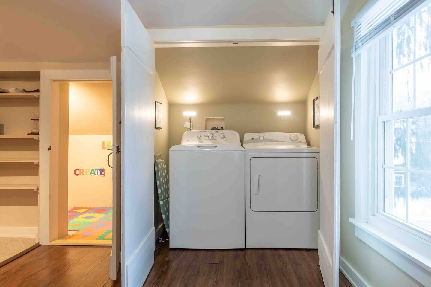 A laundry room with two washing machines, a drying machine, and a door leading to a hallway with a colorful rug.