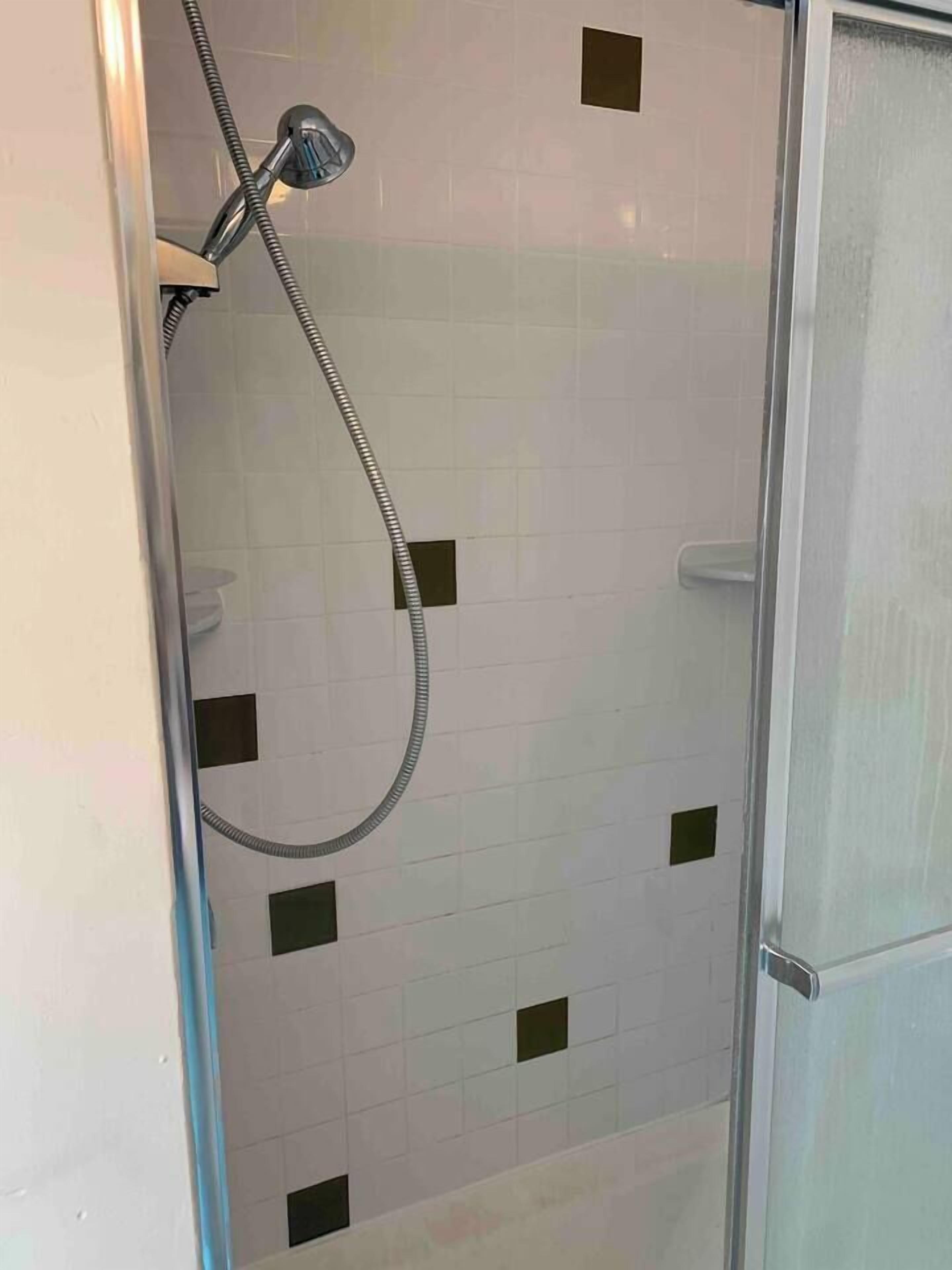 Eine Dusche mit Glastür, weißen Fliesenwänden und schwarzen quadratischen Fliesen.