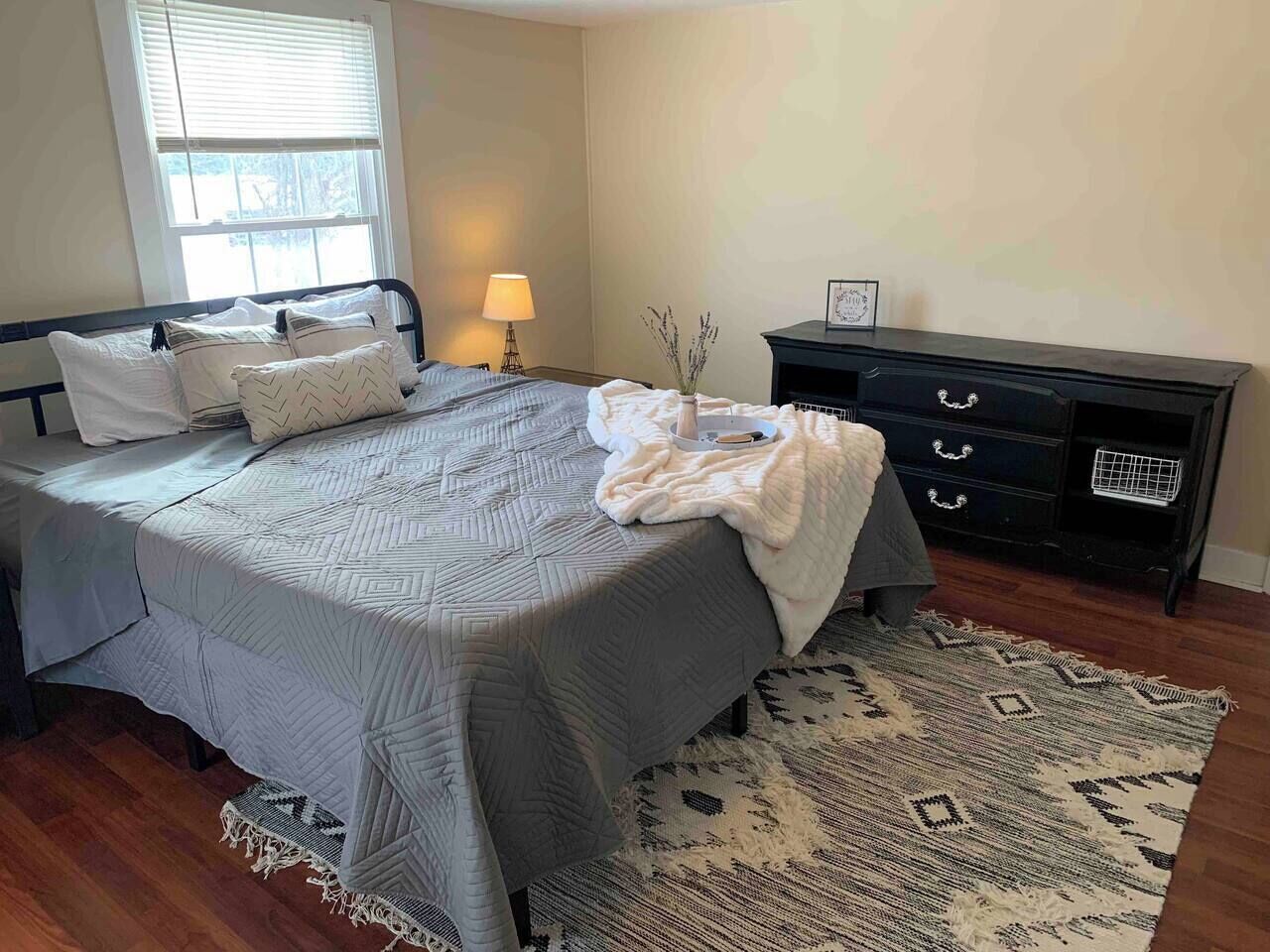 A bedroom with a bed, bedside lamp, dresser, and a patterned rug.