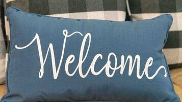 Een blauw rechthoekig kussen met de tekst 'Welcome' geborduurd in witte sierletters.