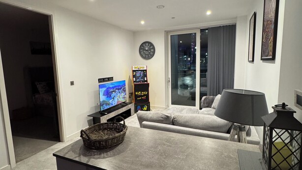 Una sala de estar moderna con un televisor de pantalla plana, una consola de videojuegos, un sofá y un comedor con una lámpara y un farol.