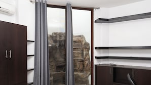Ein Zimmer mit Steinwand, einer Schiebetür mit grauen Vorhängen, einem dunklen Holzschrank und einem schwarzen Bürostuhl.