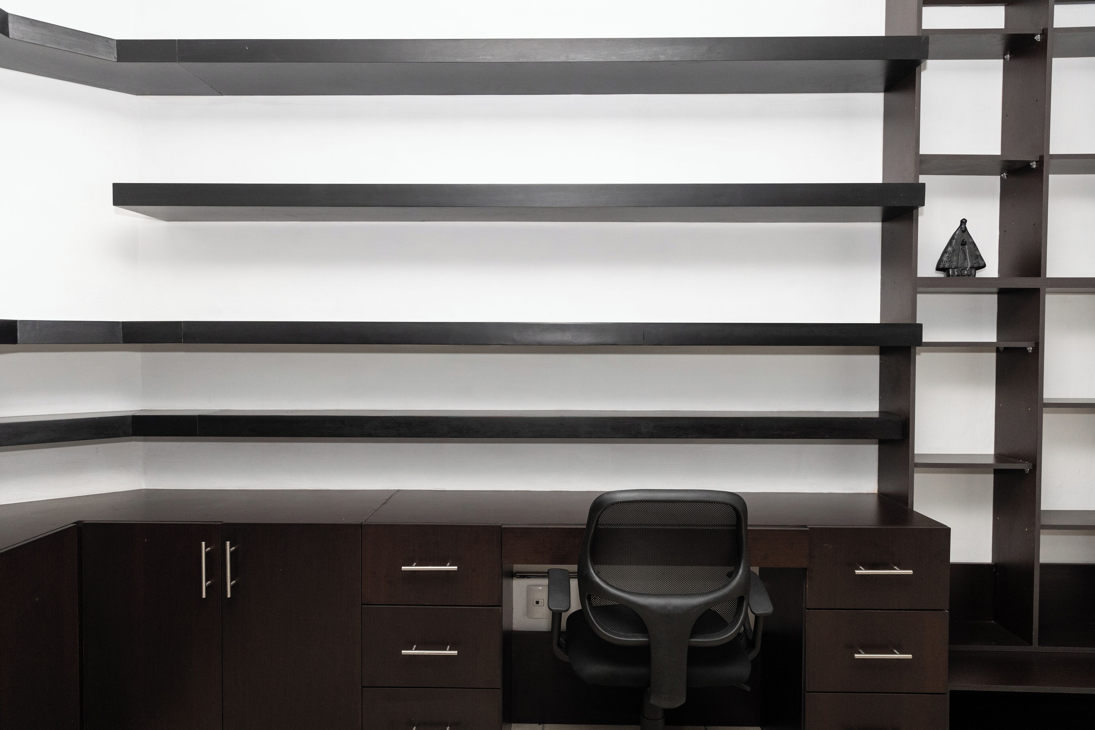 A modern office space with a dark wood desk, a black office chair, and built-in shelving.