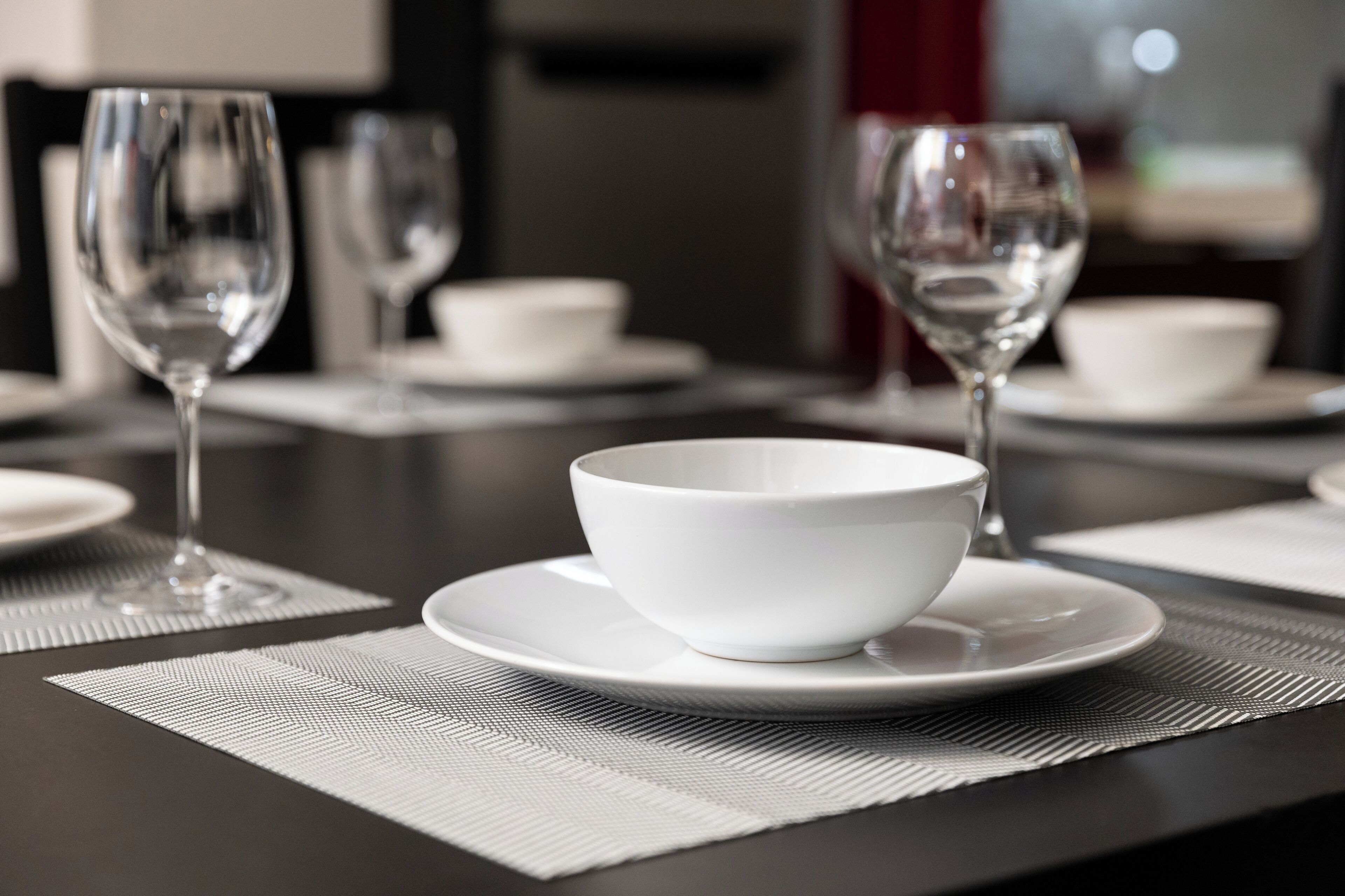 A dining table with white plates, bowls, and wine glasses arranged on a dark tablecloth.