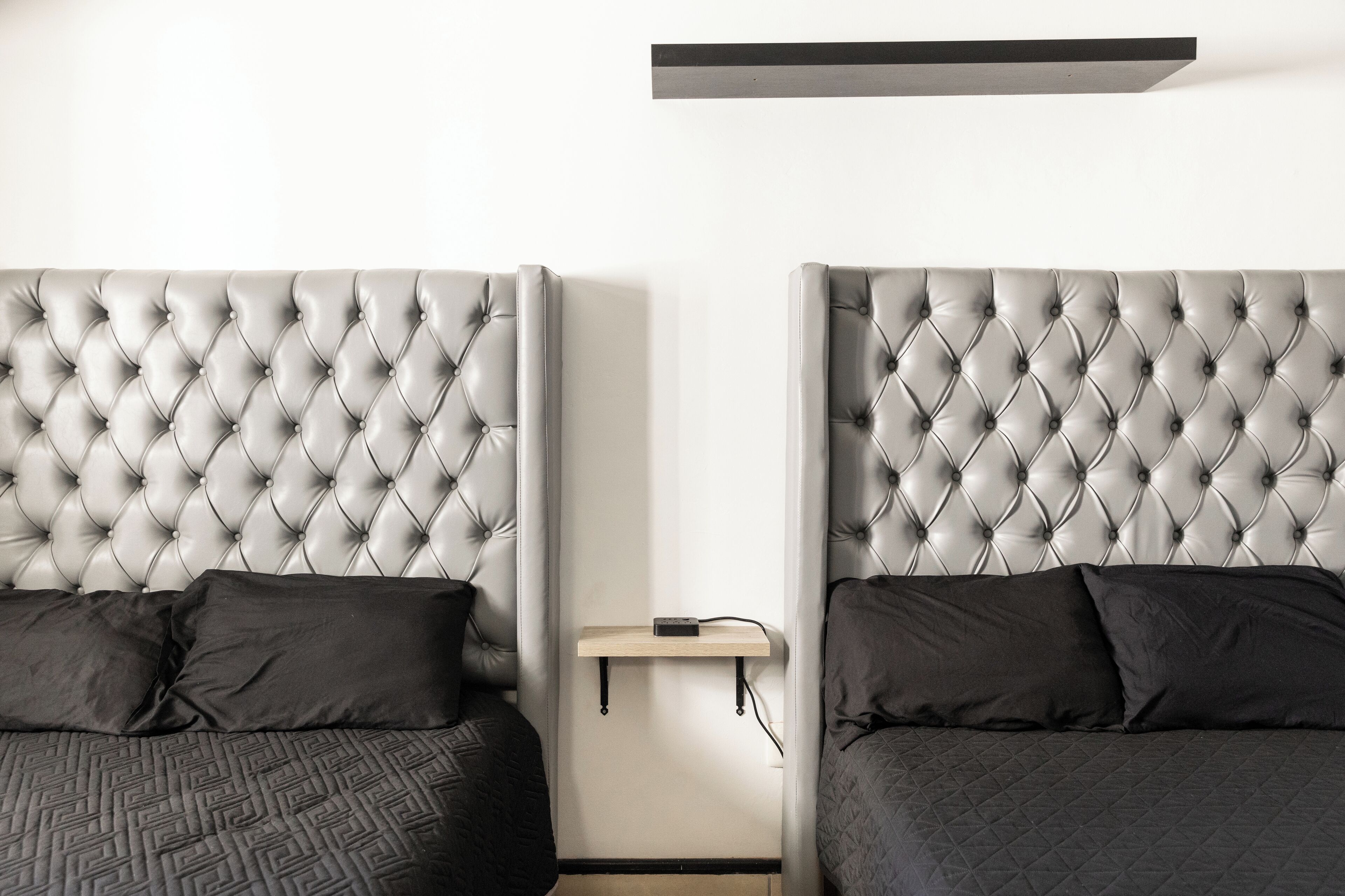 A bedroom with two beds, each with a tufted headboard, a bedside table, and a shelf above the beds.