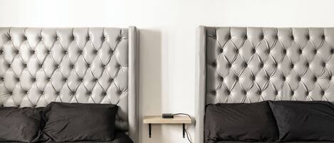 A bedroom with two beds, each with a tufted headboard, a bedside table, and a shelf above the beds.
