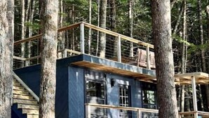 A cabin with a wooden staircase leading to a deck, surrounded by trees. - Come play in the water at this secluded get away.
Observe nature at its best.
 (Little Ridge)