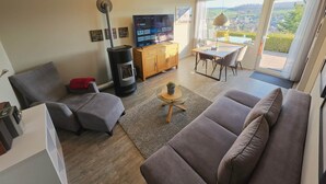 A modern living room with a sofa, a TV, a fireplace, and a dining area with a table and chairs. - Your getaway! Cozy - Nature - Panoramic views! (Lichtenau)
