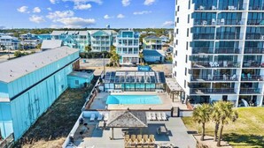A coastal hotel with a pool area, multiple buildings, and a clear sky.