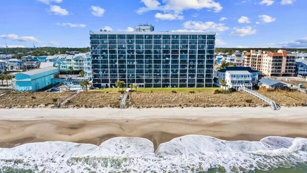 A beachfront hotel with a modern glass building, a sandy beach, and a view of the ocean.