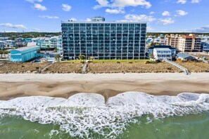 Un hôtel situé en bord de mer, doté d’un bâtiment moderne en verre, d’une plage de sable et offrant une vue sur l’océan.