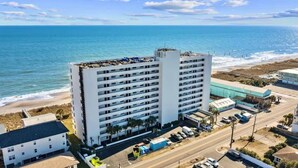A multi-story hotel with a beach view, located near a coastal road with parked vehicles.