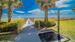 A wooden boardwalk leading to a beach with palm trees and a clear sky.