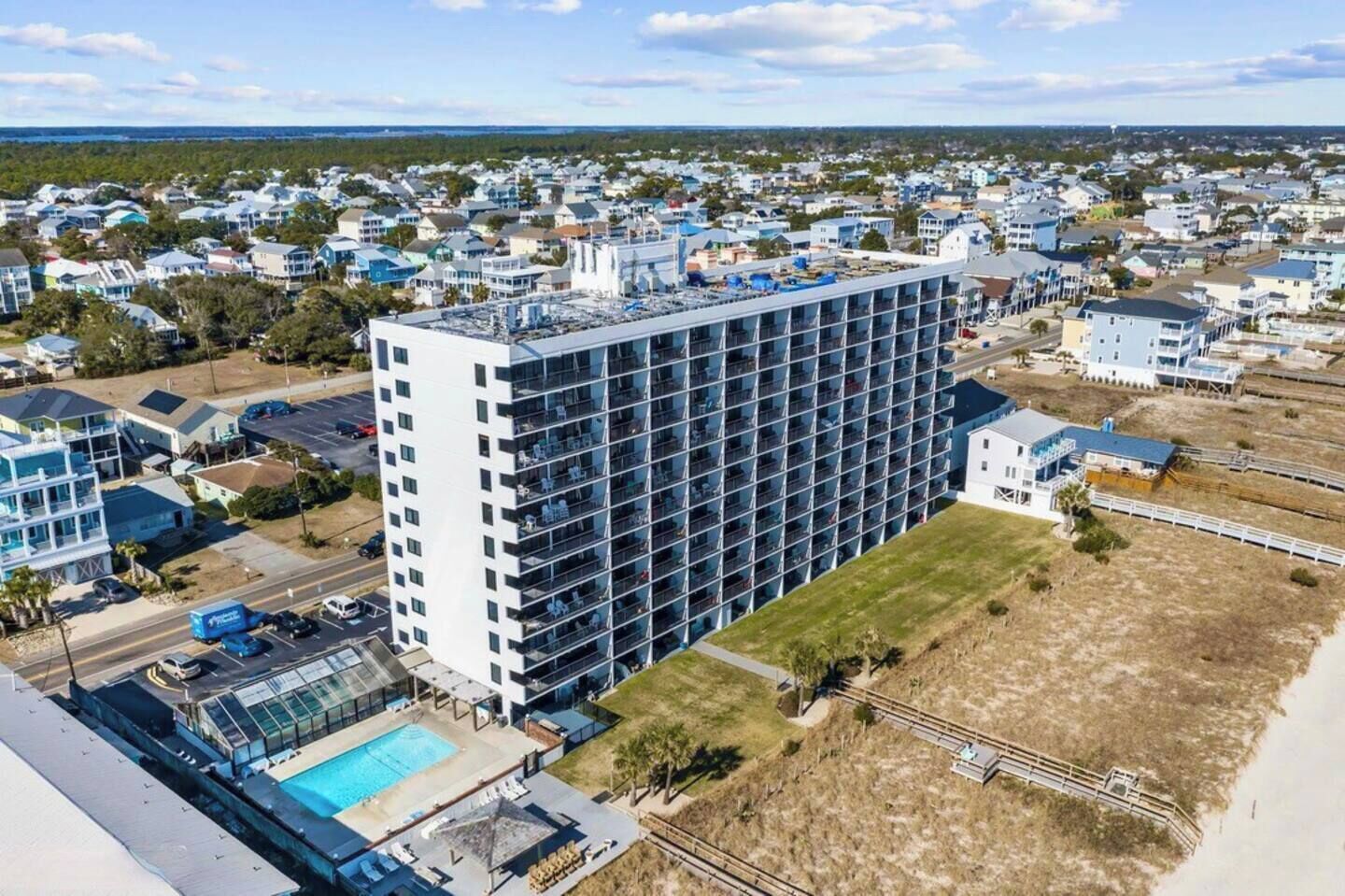 A high-rise hotel with multiple floors, a swimming pool, and a beach view.
