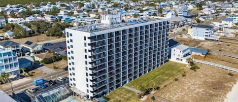 A high-rise hotel with multiple floors, a swimming pool, and a beach view.