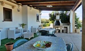 An outdoor patio with wicker furniture, a table with a fruit bowl, and a stone oven.