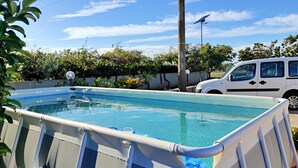 Piscina com deck revestido, rodeada por vegetação e uma van estacionada.