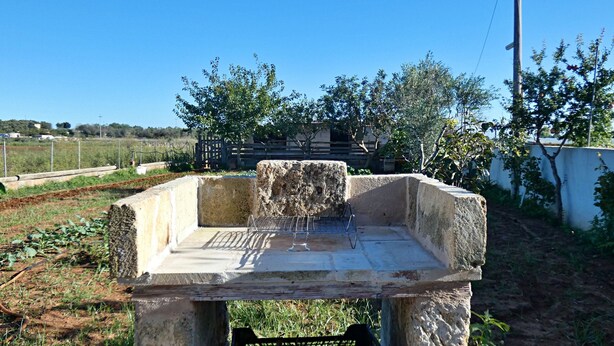 Estrutura de pedra com grade metálica no centro, rodeada por vegetação e cercada por uma vedação em ambiente rural.