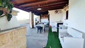 An outdoor patio area with a stone ledge, a table with chairs, a sofa, and a small table with a plant.