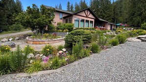 A building with a garden in front, surrounded by trees. - Mara Spring Lodges - Suite 2 (Mara)