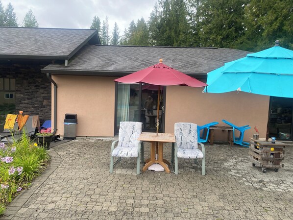A patio with a table and chairs, a red umbrella, and a blue umbrella. - Mara Spring Lodges - Suite 2 (Mara)