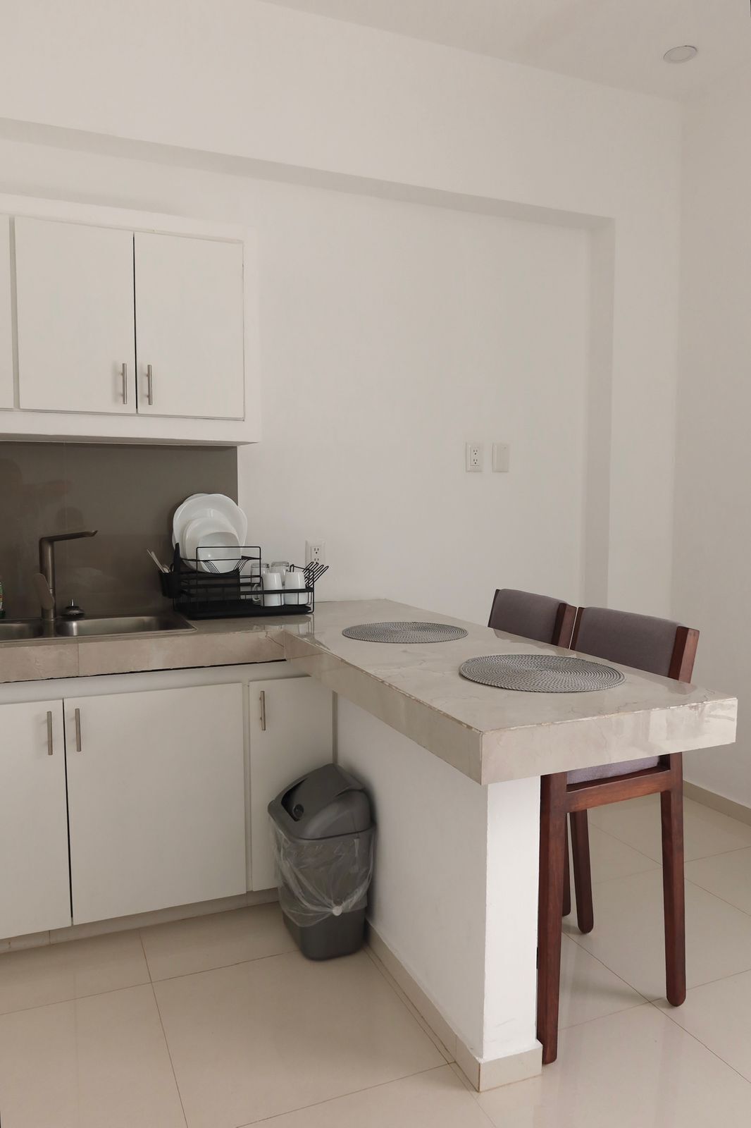 Una cocina moderna con armarios blancos, un lavamanos de acero inoxidable y una zona de comedor con mesa y sillas.