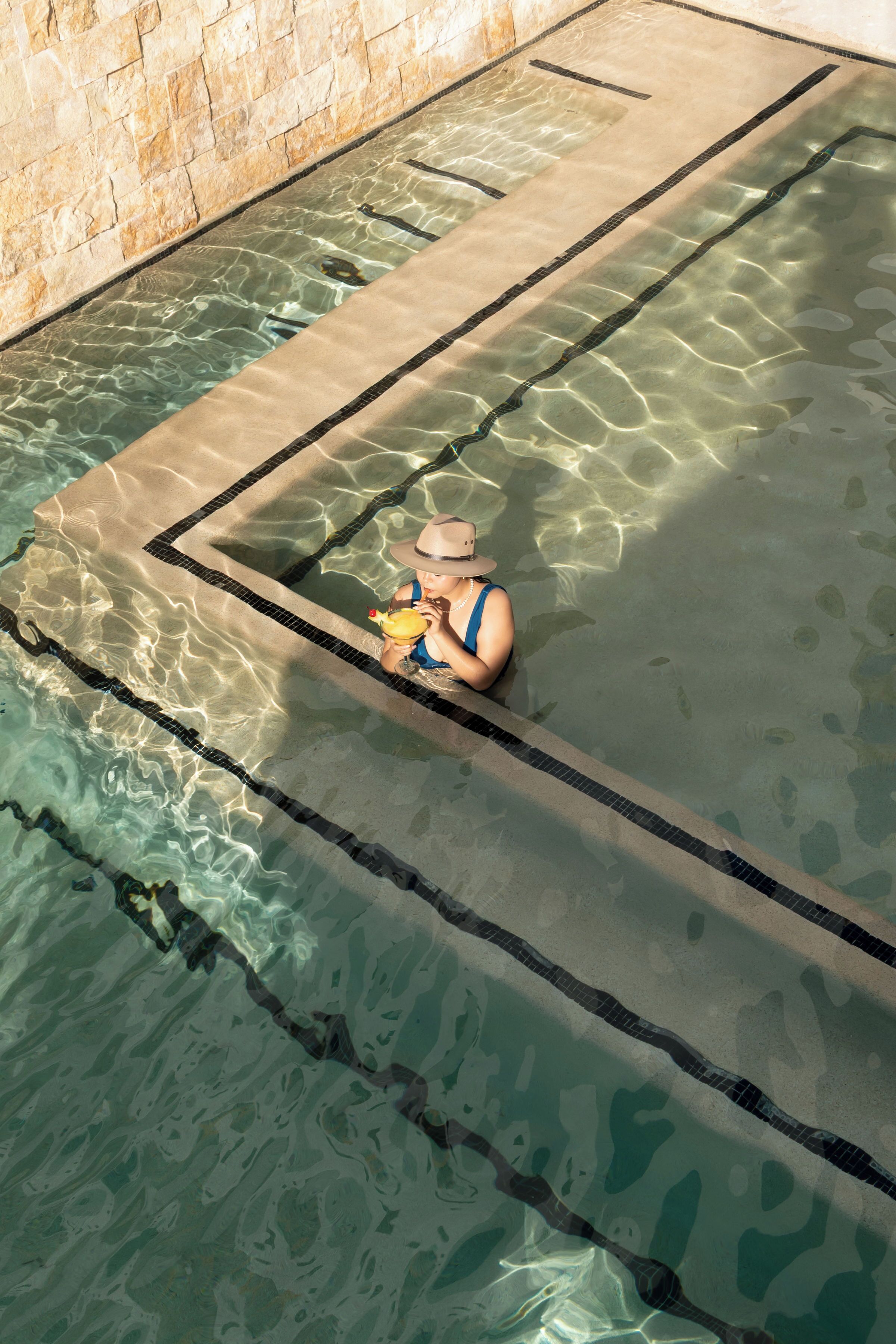 Une piscine à l’eau claire, une terrasse carrelée et un mur en pierre.