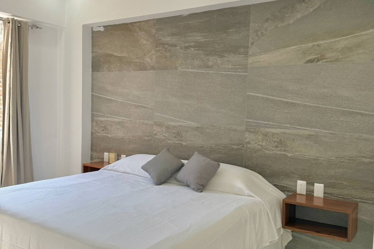 A modern bedroom with a large bed, a ceiling fan, and a textured wall.