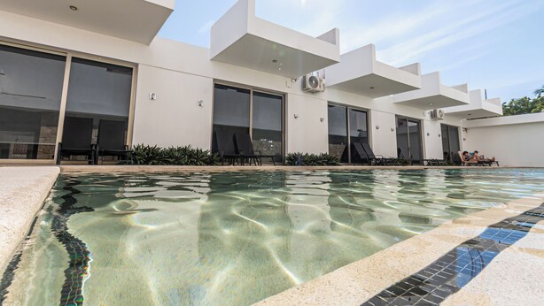 Un edificio moderno con piscina, ventanas amplias y mobiliario exterior.