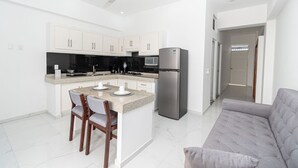Una cocina moderna con armarios blancos, un refrigerador de acero inoxidable y una zona de comedor con dos sillas.