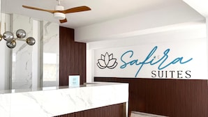 Una moderna zona de recepción con mostrador de mármol, ventilador de techo y un cartel en la pared para Safira Suites.