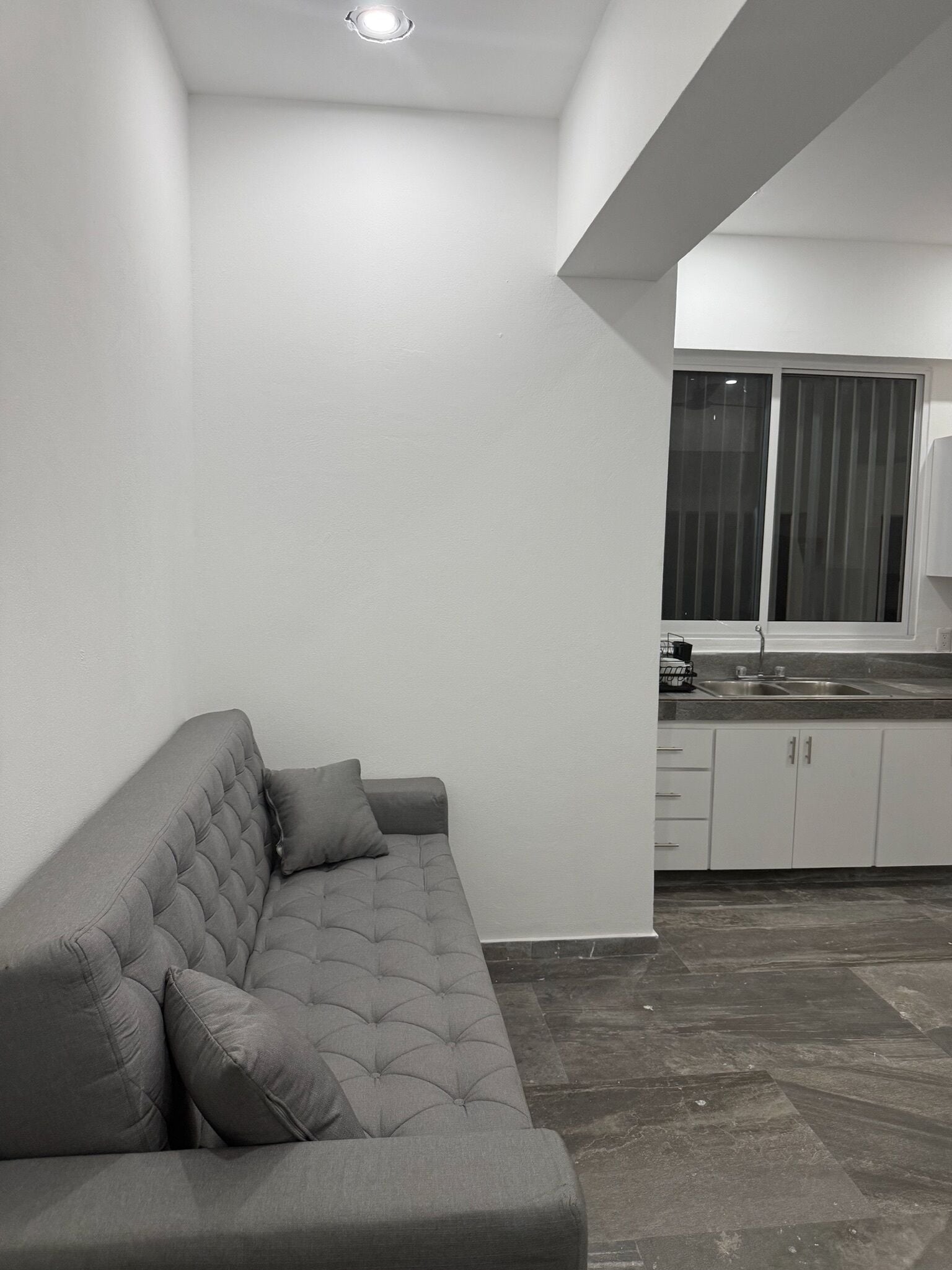Un salón moderno con un sofá gris y una cocina visible al fondo.