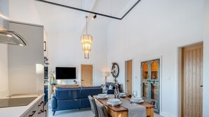 A modern kitchen with a built-in oven, a dining area with a wooden table and chairs, a blue sofa, and a TV mounted on the wall. - Moorgate Lodge - UK47742 (Kelbrook)