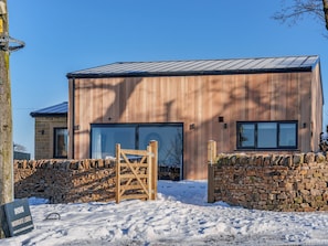 Un bâtiment moderne avec une entrée ornée d’un mur en pierre, une porte en bois et un sol recouvert de neige.