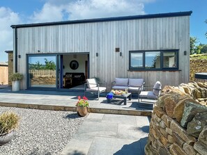 A modern building with a large sliding glass door entrance, outdoor seating area with a sofa and chairs, and a stone wall in the background. - Moorgate Lodge - UK47742 (Kelbrook)