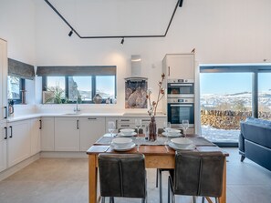 A modern kitchen with a dining area, large windows, and a view of the countryside.