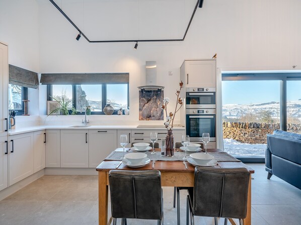 A modern kitchen with a dining area, large windows, and a view of the countryside.