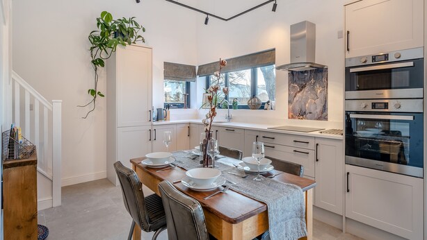 A modern kitchen with white cabinetry, a dining table set for four, and a large window providing natural light. - Moorgate Lodge - UK47742 (Kelbrook)