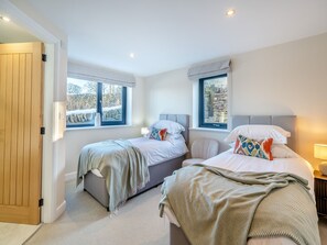 A bedroom with two beds, a wooden door, and windows with views of a stone wall and trees.