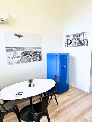 A room with a round table, two chairs, a blue refrigerator, and two black-and-white photographs on the walls. - Courtyard View At The Commons - Dog Friendly (Seaside)