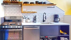 Eine kompakte Küche mit Herd, Backofen und Geschirrspüler, einem Spülbecken sowie einer Kaffeemaschine.