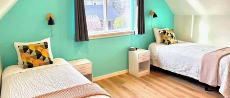 A bedroom with two beds, a window with curtains, a bedside table, and a nightstand.
