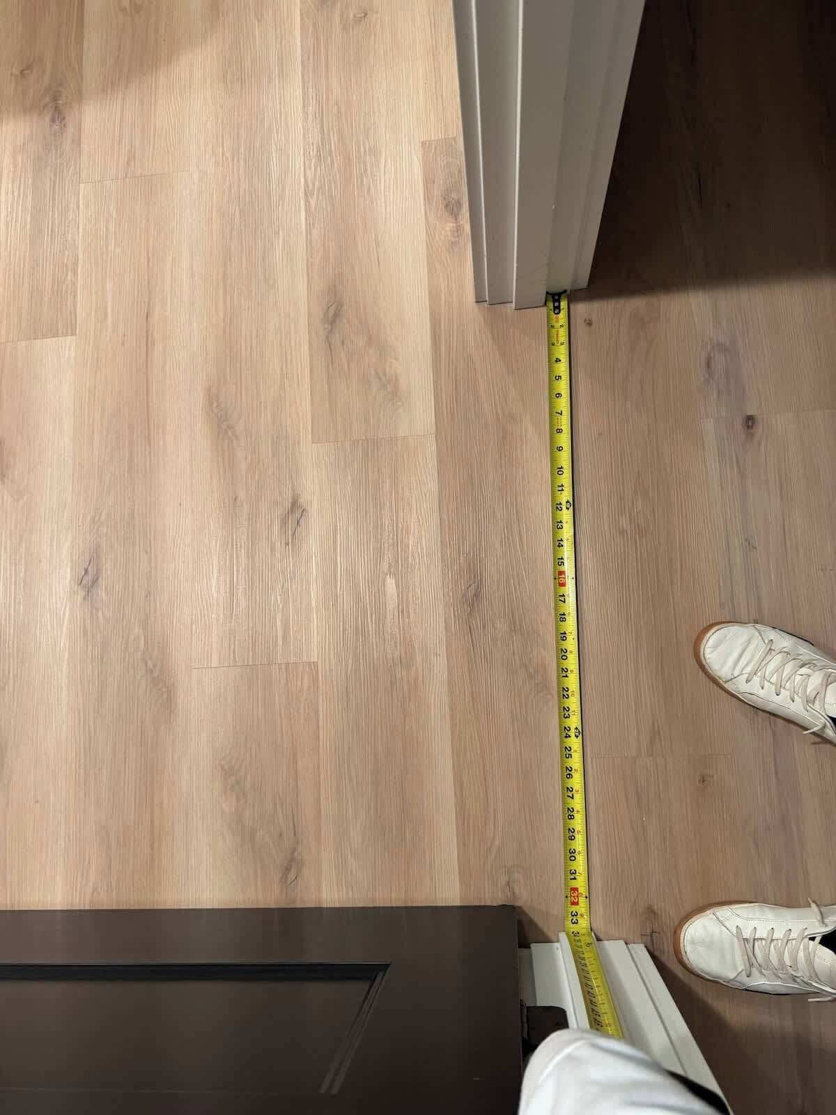 A wooden floor with a measuring tape and a pair of white sneakers.