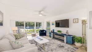 A spacious living room with a large window, a ceiling fan, a flat-screen TV, and a coffee table. - Discover the perfect getaway at Villa De Marco East, (Marco Island)