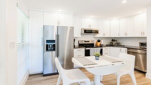A modern kitchen with white cabinetry, stainless steel appliances, and a dining area with a white table and chairs. - Discover the perfect getaway at Villa De Marco East, (Marco Island)