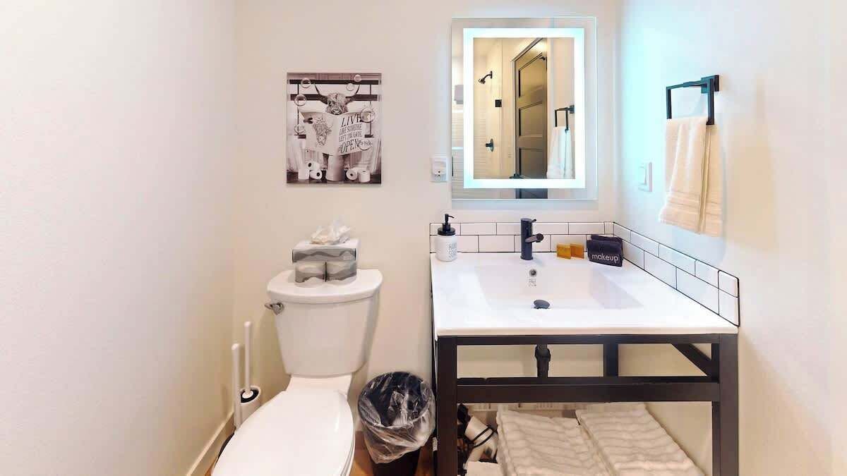 Ein Badezimmer mit einer weißen Toilette, einem Waschbecken mit schwarzem Rahmen, einem Spiegel über dem Waschbecken und einem Handtuchhalter an der Wand.