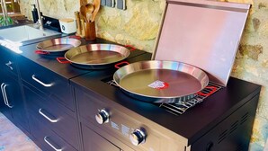 A kitchen with a stone wall, a sink, and a stove with two frying pans. - Village house in Palamós (Palamós)