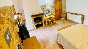 A rustic bedroom with exposed beams, a stone wall, a wooden bed, a small table with a mirror, and a radiator. - Village house in Palamós (Palamós)